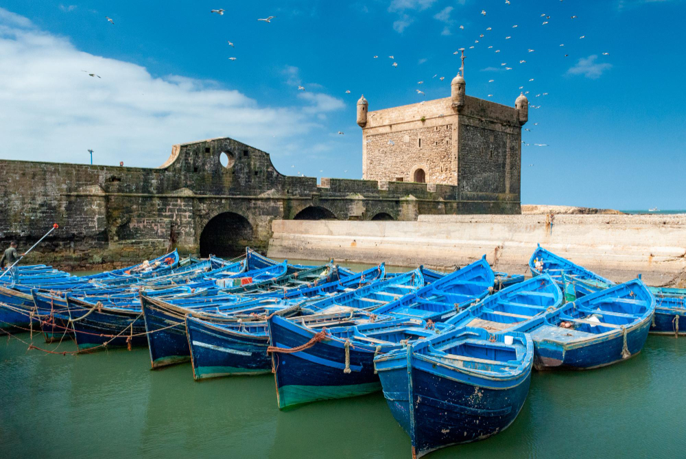 View of the charming port of Essaouira, with fishing boats docked in the harbor and the historic fortress in the background, in Morocco.