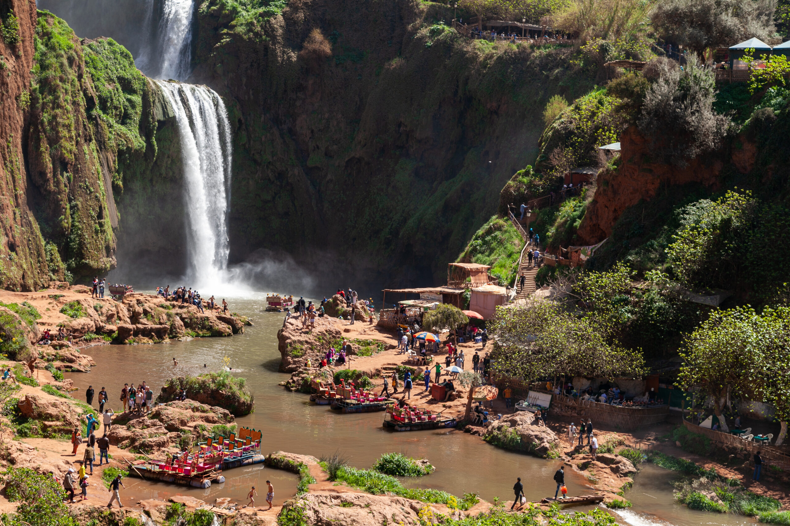 Stunning view of the Ouzoud Waterfalls, cascading down rocky cliffs surrounded by lush greenery and pools, in Morocco.