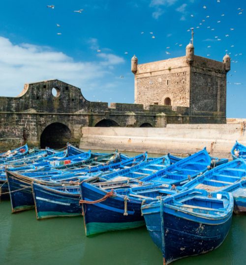 View of the charming port of Essaouira, with fishing boats docked in the harbor and the historic fortress in the background, in Morocco.