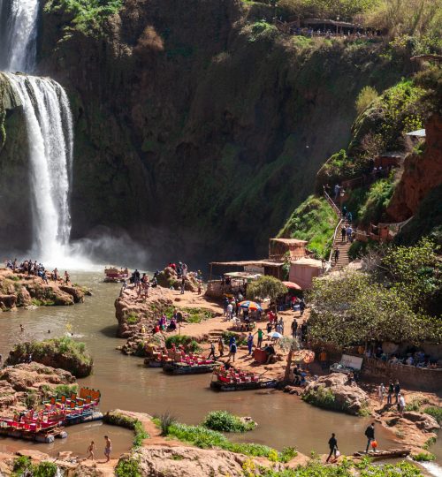 Stunning view of the Ouzoud Waterfalls, cascading down rocky cliffs surrounded by lush greenery and pools, in Morocco.